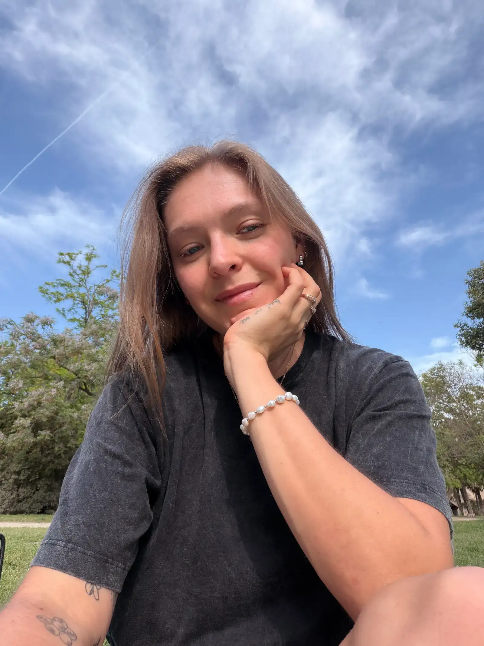 Victoria, the coach, smiling outdoors in a park with trees and a blue sky behind her